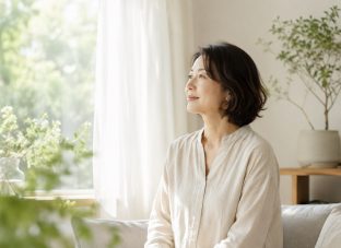 窓辺で外を眺めながら静かに気持ちを整える40代50代女性