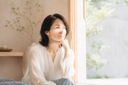 窓辺でやわらかな光を浴びながら、静かにこれからを見つめる40代後半から50代前半の女性