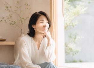 窓辺でやわらかな光を浴びながら、静かにこれからを見つめる40代後半から50代前半の女性