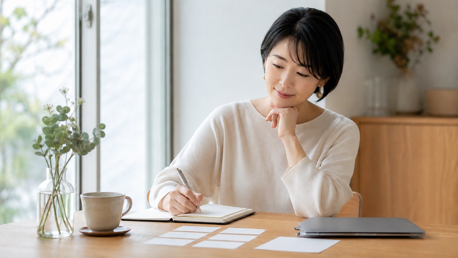 アラフィフ女性が、明るい室内のテーブルでノートに書きながら、これからの働き方を整理している様子