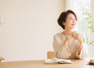 窓辺でカップを手に、穏やかな時間を過ごすアラフィフ女性
