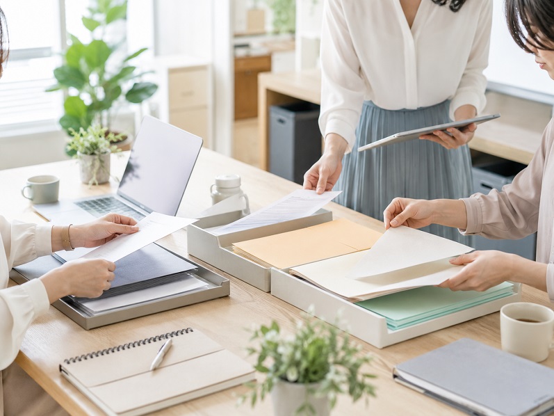 オフィスで書類を整理しながら業務分担を見直す女性たち